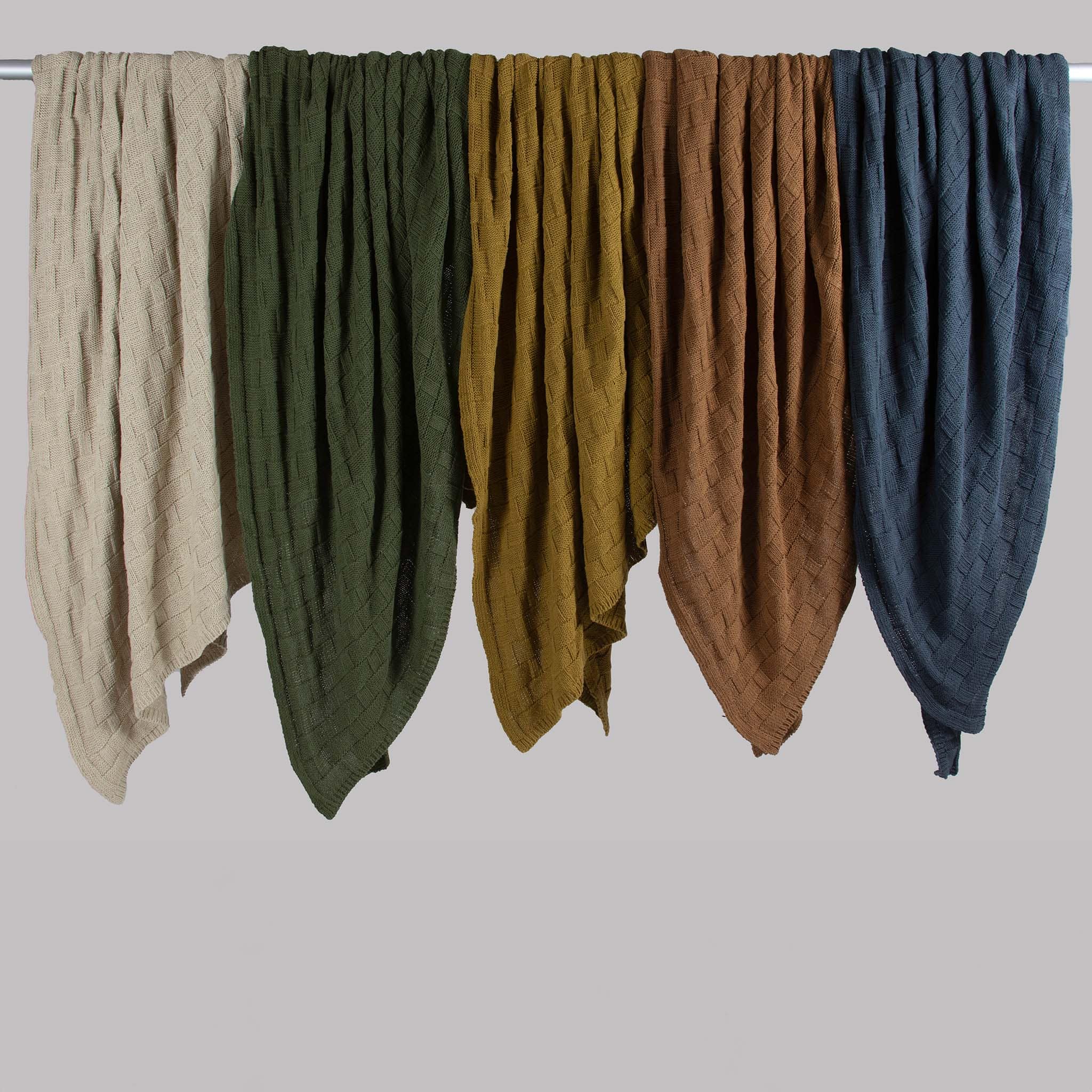 Five in2green Basketweave Throw Blankets, made from sustainable recycled yarns, hang side by side in cream, dark green, olive, brown, and blue against a plain background.