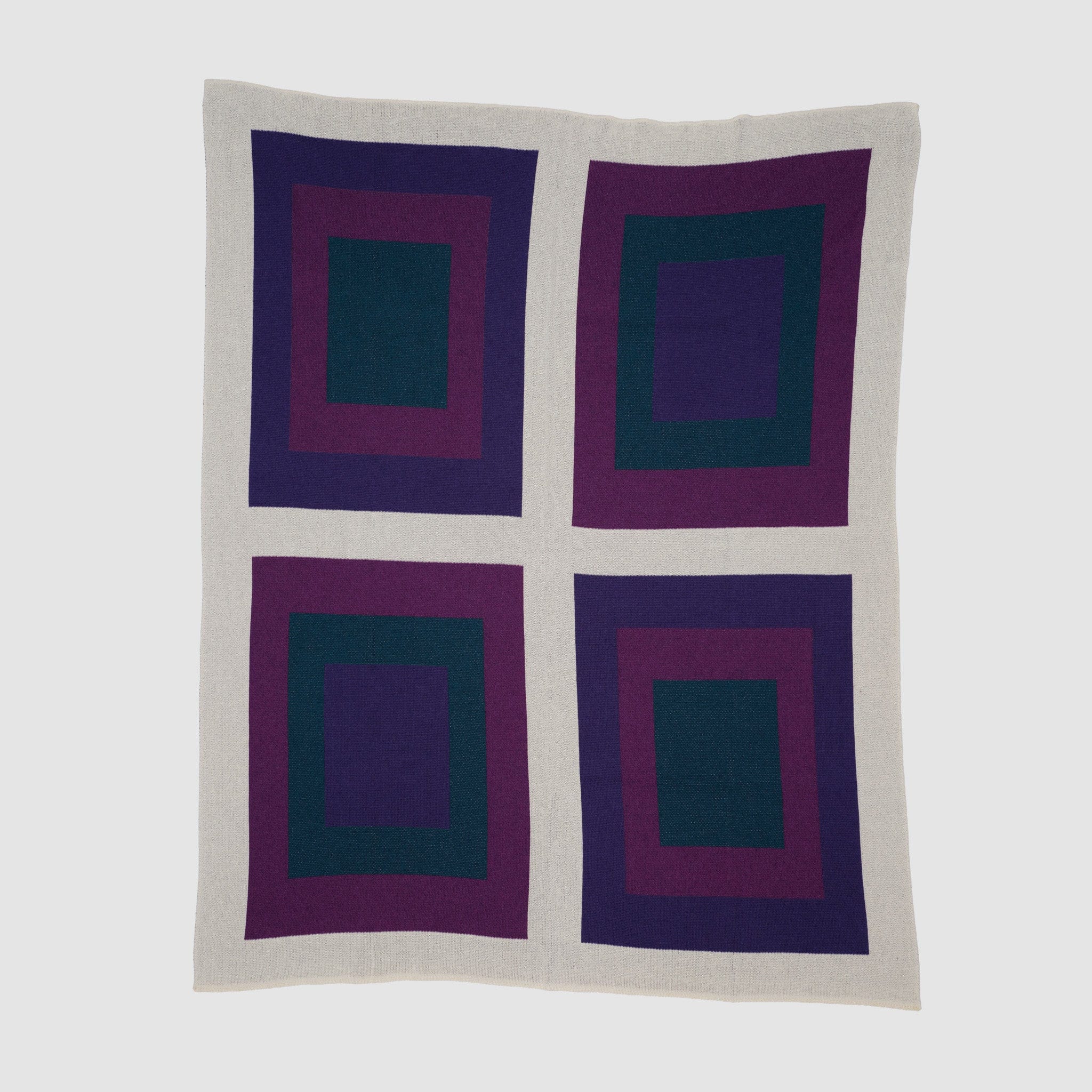 The Bauhaus Throw Blanket features four large square blocks with nested squares in dark green, purple, and burgundy on a light gray background—an iconic Bauhaus-inspired design.