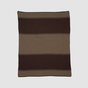The Block Canyon Throw Blanket, knitted from sustainable recycled yarns, displays wide dark brown and light brown horizontal stripes and is shown laid flat on a light background.