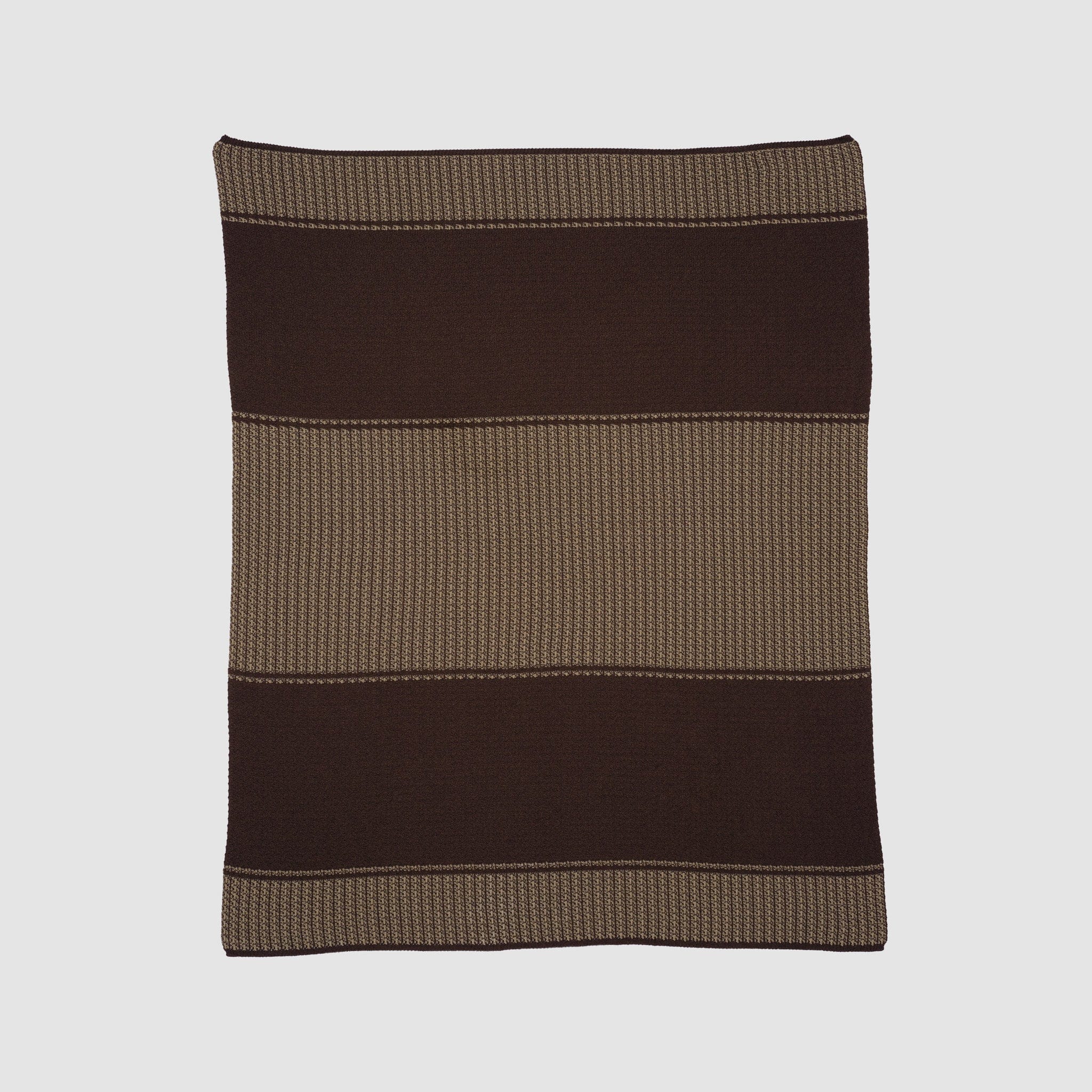 The Block Canyon Throw Blanket, knitted from sustainable recycled yarns, displays wide dark brown and light brown horizontal stripes and is shown laid flat on a light background.