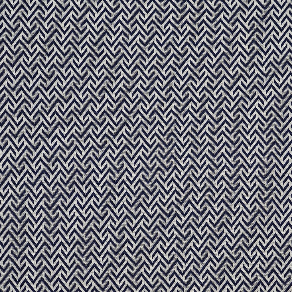 A close-up of the in2green Broken Zig Zag Throw Blanket showcases its repeating navy blue and white geometric zigzag pattern, reminiscent of a chevron design.