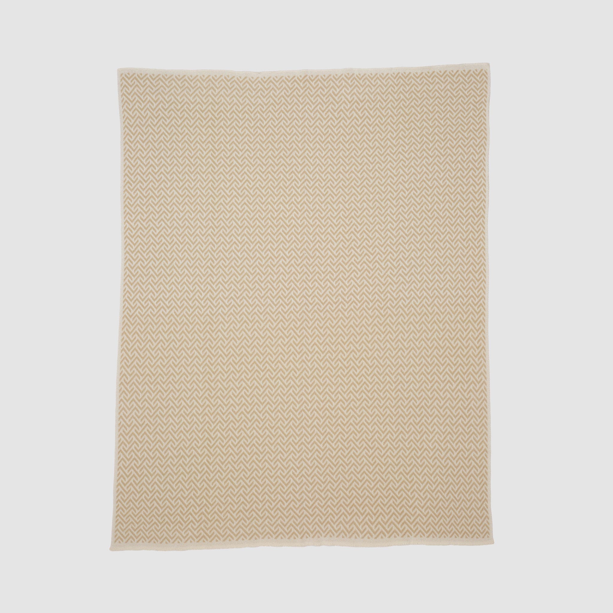 The Broken Zig Zag Throw Blanket is a beige, rectangular blanket with a repeating chevron pattern, made from recycled cotton yarns and shown laid flat on a plain white background.