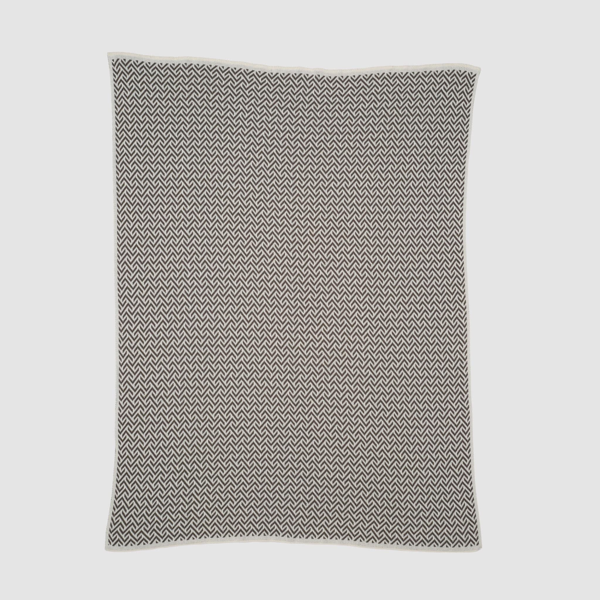 The Broken Zig Zag Throw Blanket, made from recycled cotton yarns and featuring a black and white chevron pattern, is shown flat on a white background.