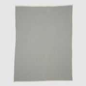 The Checkerboard Throw Blanket is a rectangular, light grey mini throw made from sustainable upcycled cotton with a subtle geometric pattern and off-white edges—perfect for cozy living and displayed on a plain background.