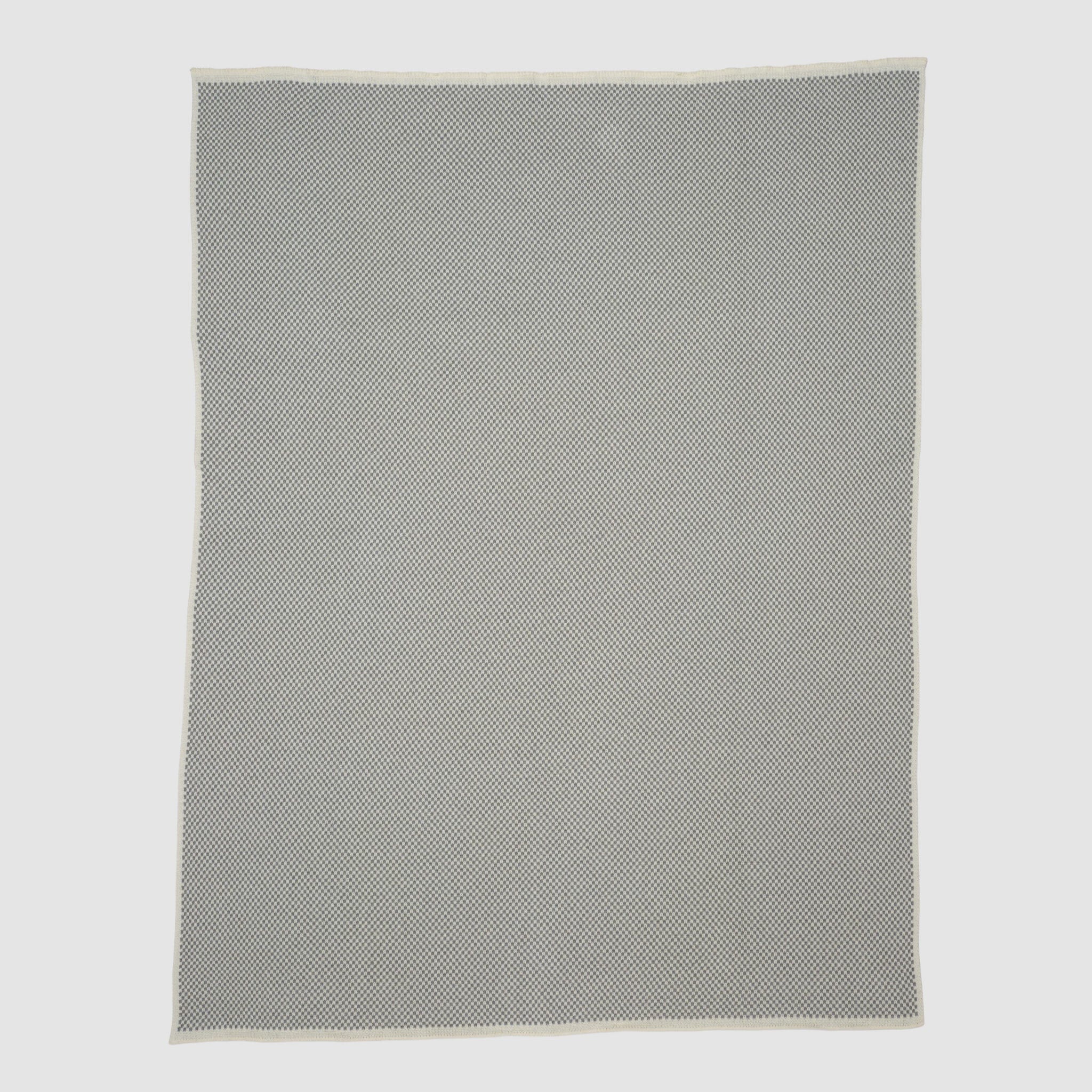The Checkerboard Throw Blanket is a rectangular, light grey mini throw made from sustainable upcycled cotton with a subtle geometric pattern and off-white edges—perfect for cozy living and displayed on a plain background.