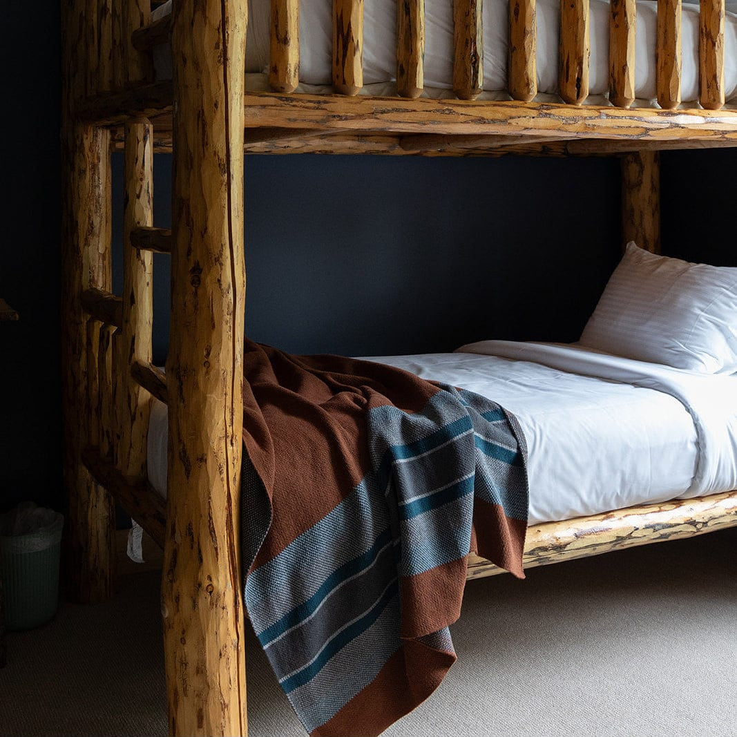 A wooden bunk bed with white bedding and a Lodge Stripe Throw Blanket draped over the lower bunk, set against a dark wall in a cozy room.