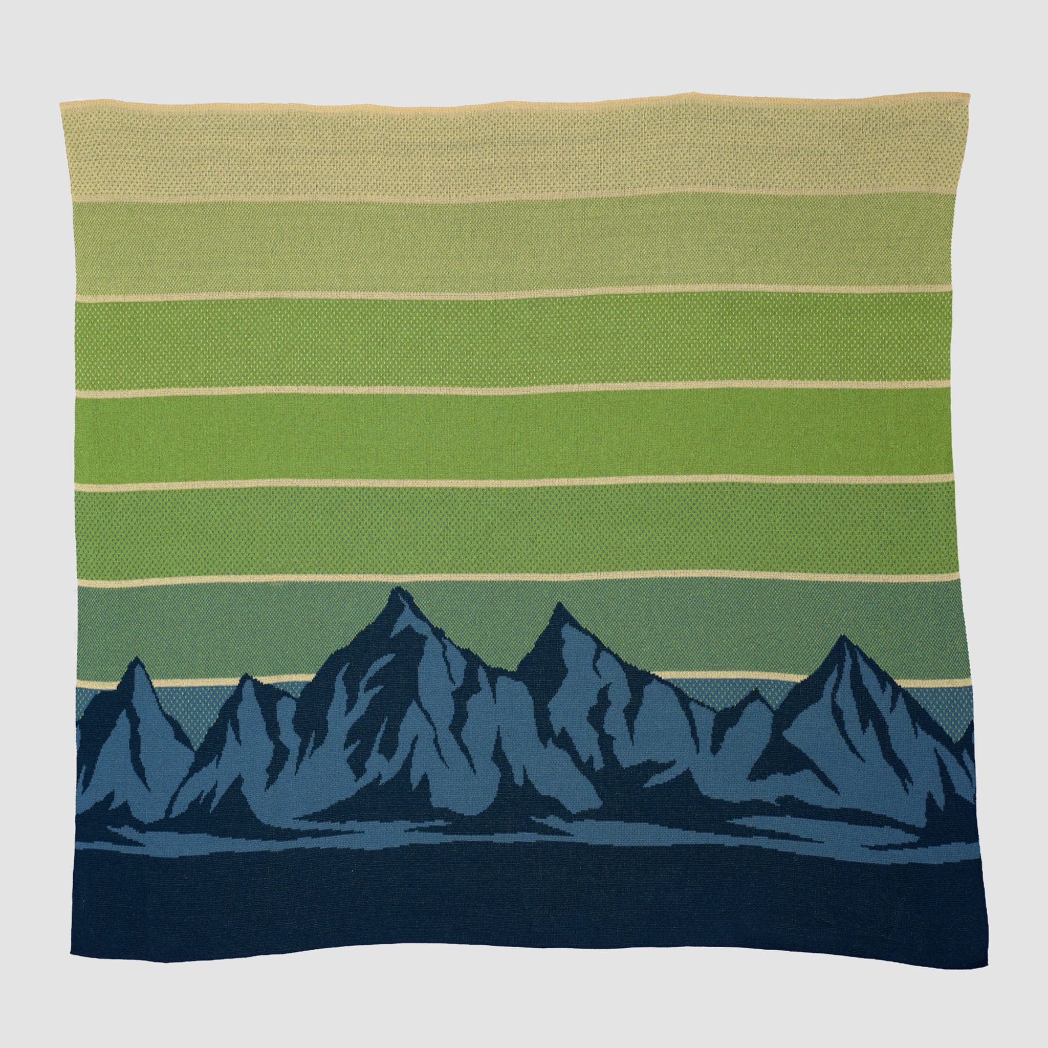 The Mountain Sunscape Throw Blanket is a sustainable knit with horizontal green stripes above a dark blue mountain range design on a light background, inspired by the Eco Mountain Sunscape.