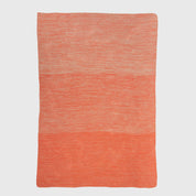 The in2green Textured Ombre Throw Blanket features a rectangular, ribbed design in two-tone orange, woven from recycled cotton and displayed flat on a white background.