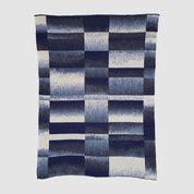 The Plaid Ombre Throw Blanket features a classic navy blue and white check with gradient squares, crafted from recycled yarn for a stylish, sustainable touch.