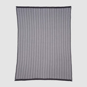 The in2green Poly Herringbone Edge Throw Blanket is a rectangular, sheer black mesh throw with vertical herringbone-knit lines and a solid black border, crafted from recycled polyester and shown flat on a plain background.
