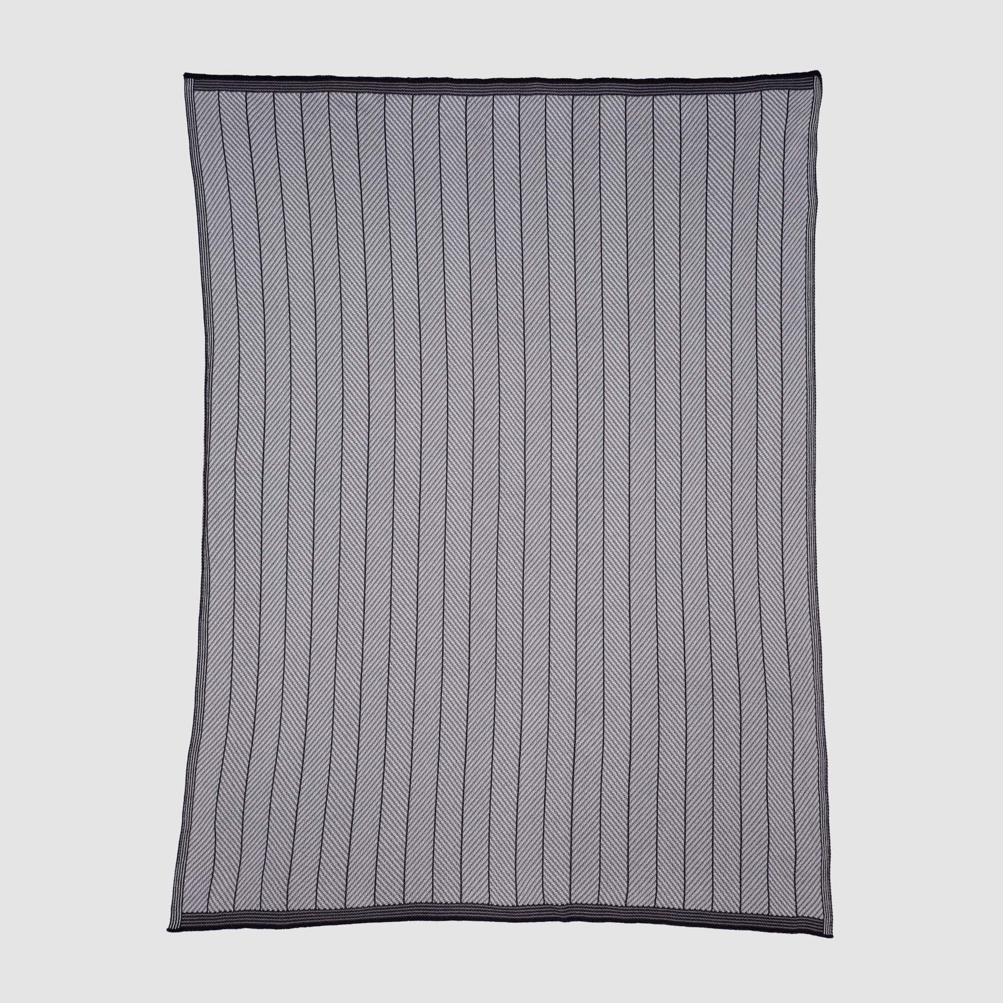 The in2green Poly Herringbone Edge Throw Blanket is a rectangular, sheer black mesh throw with vertical herringbone-knit lines and a solid black border, crafted from recycled polyester and shown flat on a plain background.