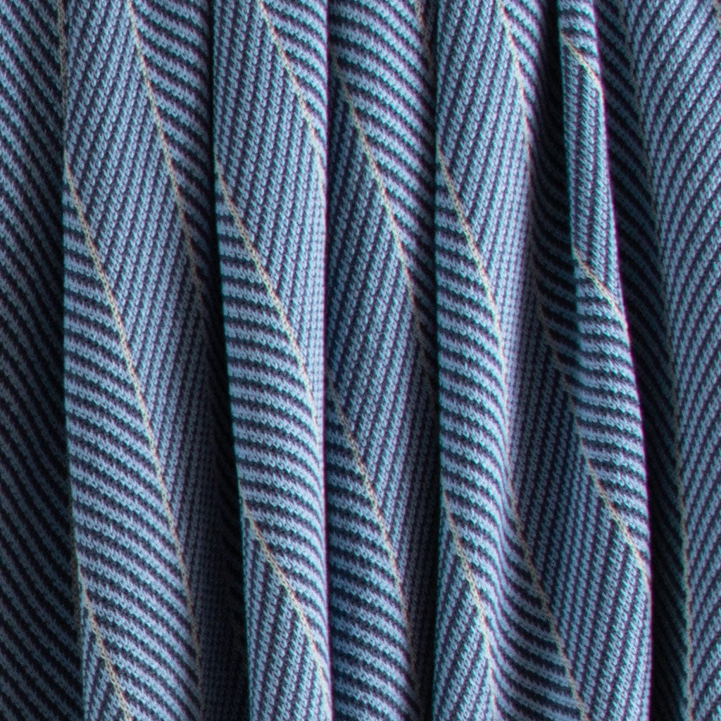 Close-up of the Poly Herringbone Edge Throw Blanket by in2green, showing blue and white recycled polyester knit with vertical folds.