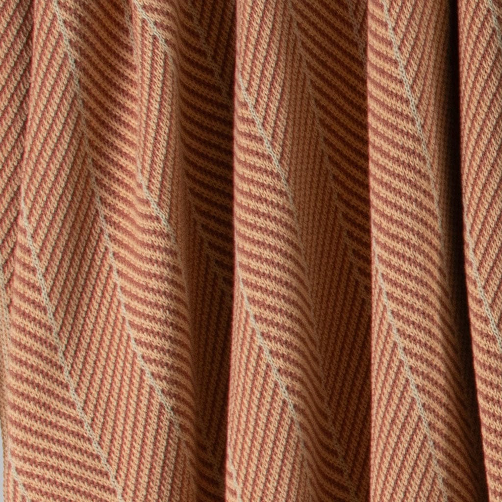 Close-up of the Poly Herringbone Edge Throw Blanket by in2green, featuring a brown and beige herringbone pattern with vertical folds, made from recycled polyester—ideal for outdoor use or cozy interiors.