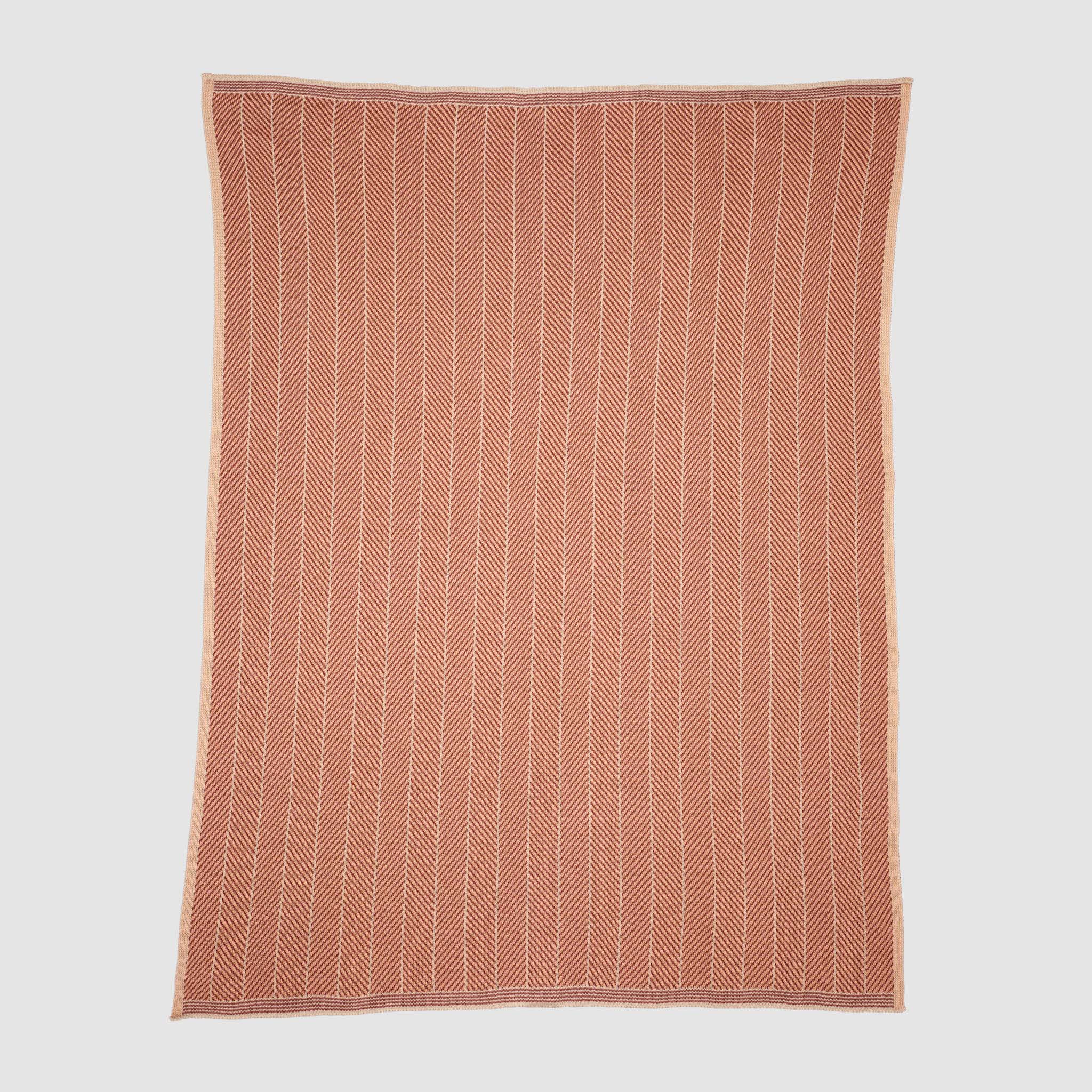 The in2green Poly Herringbone Edge Throw Blanket is a rectangular rust-colored outdoor throw with a white herringbone pattern, made from recycled polyester and shown flat on a white background.