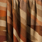 A close-up of the Southwest Arrows Throw Blanket shows pleated fabric with a diagonal plaid pattern in brown, tan, orange, and cream, inspired by Southwestern textiles for a cozy style.