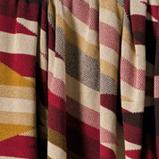A close-up of the Southwest Arrows Throw Blanket shows its cozy, textured weave and geometric pattern in red, yellow, beige, and black with diagonal lines inspired by Southwestern textiles.