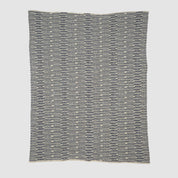 The Sand Stone Throw Blanket is a square knit with eco-friendly yarns, showcasing repeating horizontal navy blue and white earthy stripes and small rectangular shapes.