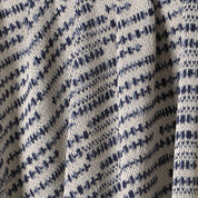 Close-up of the Sand Stone Throw Blanket, crafted from eco-friendly yarns with an irregular navy blue and white pattern that accentuates its textured knit and elegant draped folds.