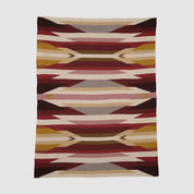 The Southwest Arrows Throw Blanket showcases a geometric pattern inspired by Southwestern textiles, with layered red, gold, beige, brown, and maroon shapes on a light background.