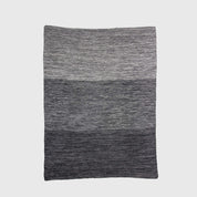The in2green Textured Ombre Throw Blanket features a subtle ribbed texture and a gradient design that shifts from light gray to dark gray, crafted from recycled cotton and shown against a plain background.