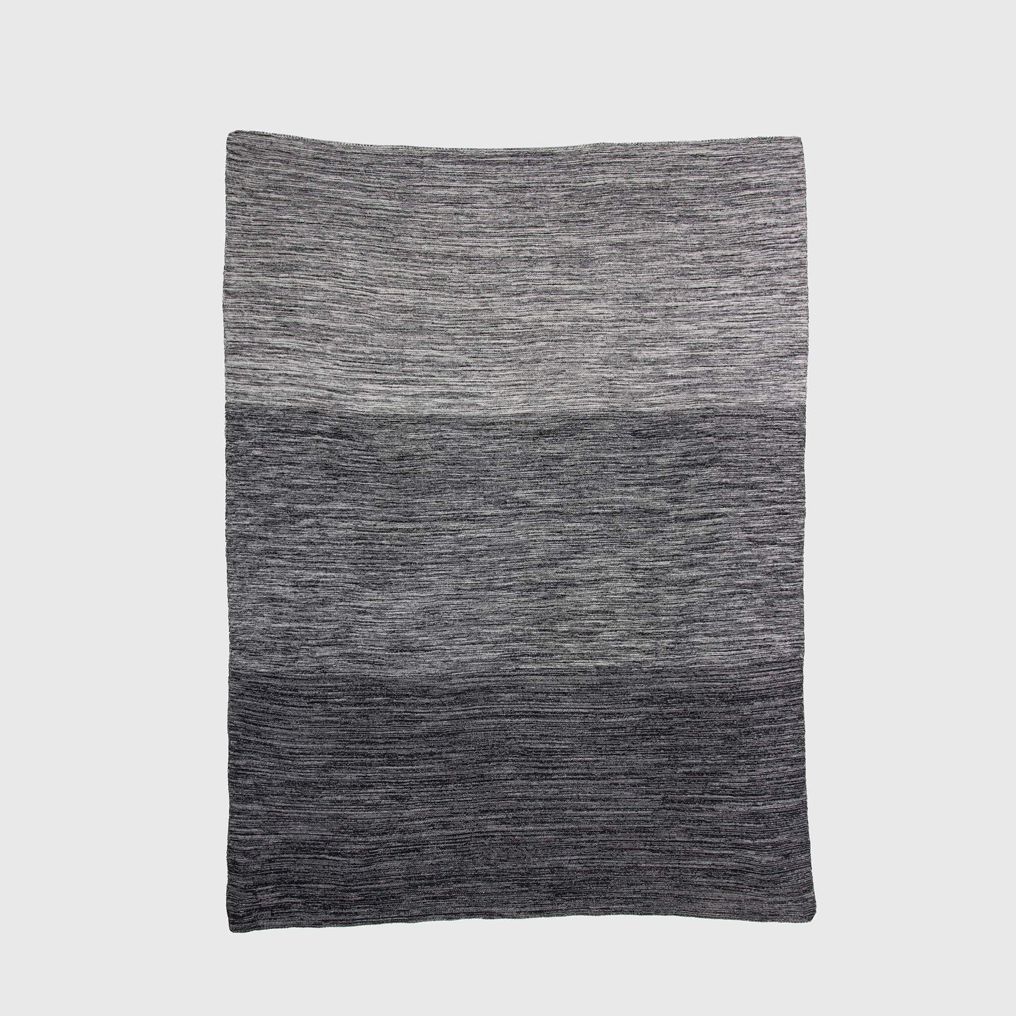 The in2green Textured Ombre Throw Blanket features a subtle ribbed texture and a gradient design that shifts from light gray to dark gray, crafted from recycled cotton and shown against a plain background.