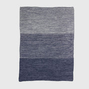 The in2green Textured Ombre Throw Blanket features a ribbed texture with horizontal color blocks in grey and blue, crafted from recycled cotton and shown on a plain white background.
