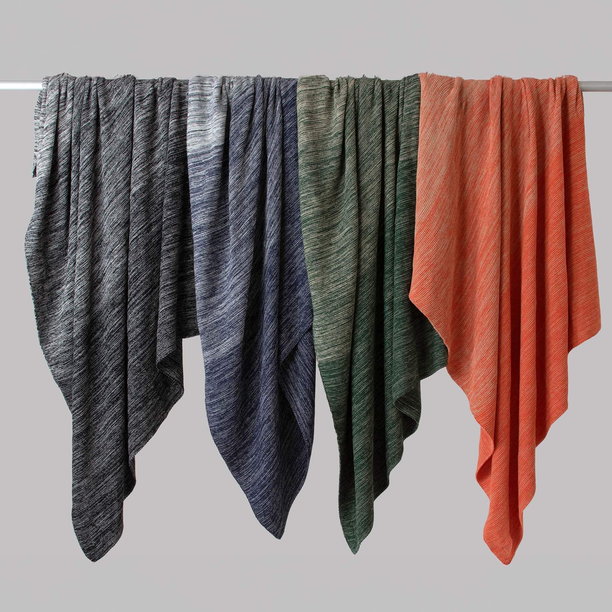 Four in2green Textured Ombre Throw Blankets in black, navy, green, and orange hang side by side on a horizontal rod against a plain gray background.