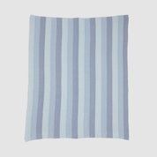 The Herringbone Hues Throw Blanket by In2Green is crafted in the USA from recycled cotton. Featuring alternating light and dark blue herringbone stripes on a white background, it combines style and sustainability for any setting.