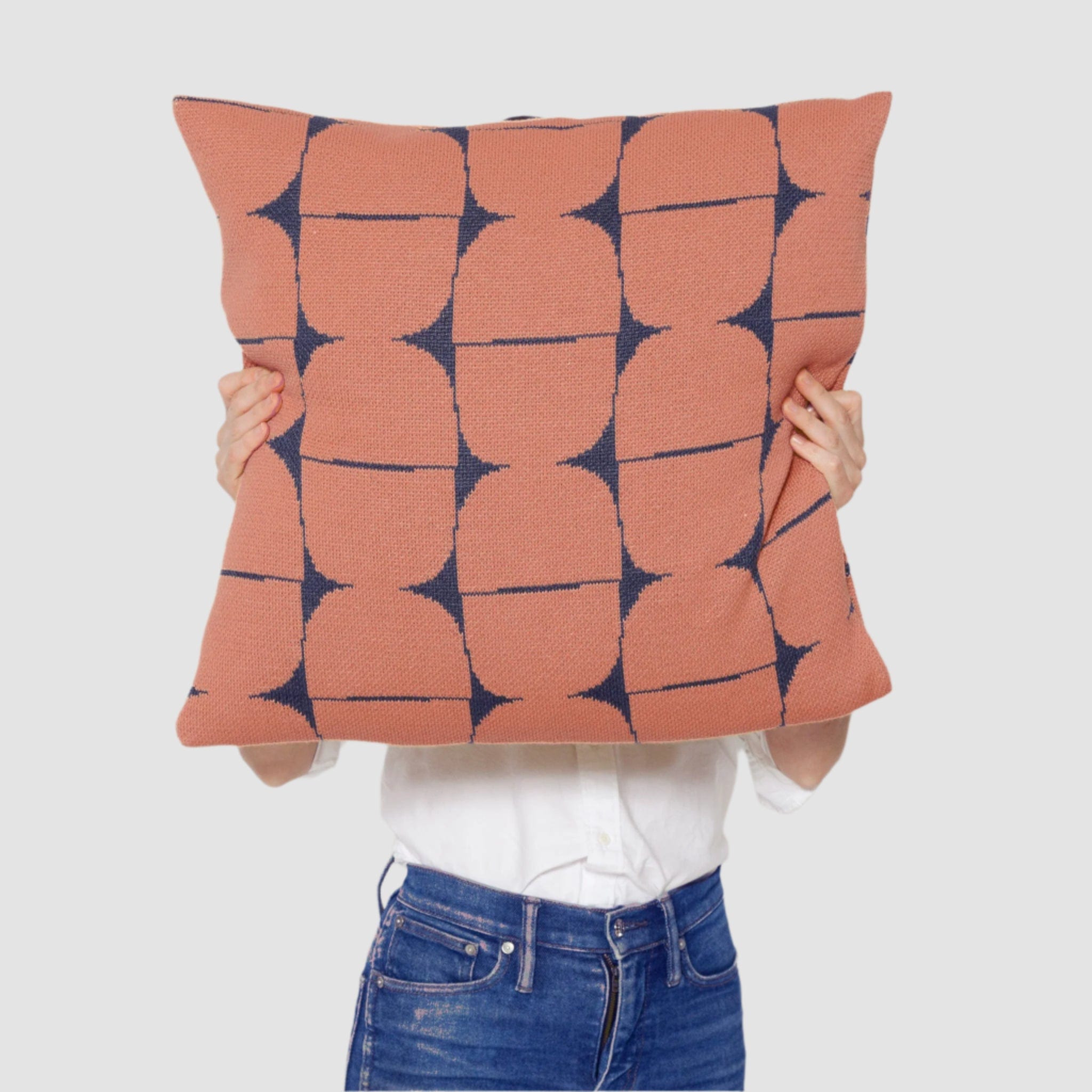A person holds the Poly Kaarna Pillow by Petra Kaksonen, showcasing a stunning geometric Nordic design. The pillow features blue and rust circles on white, crafted from recycled polyester by in2green, blending sustainability with style.