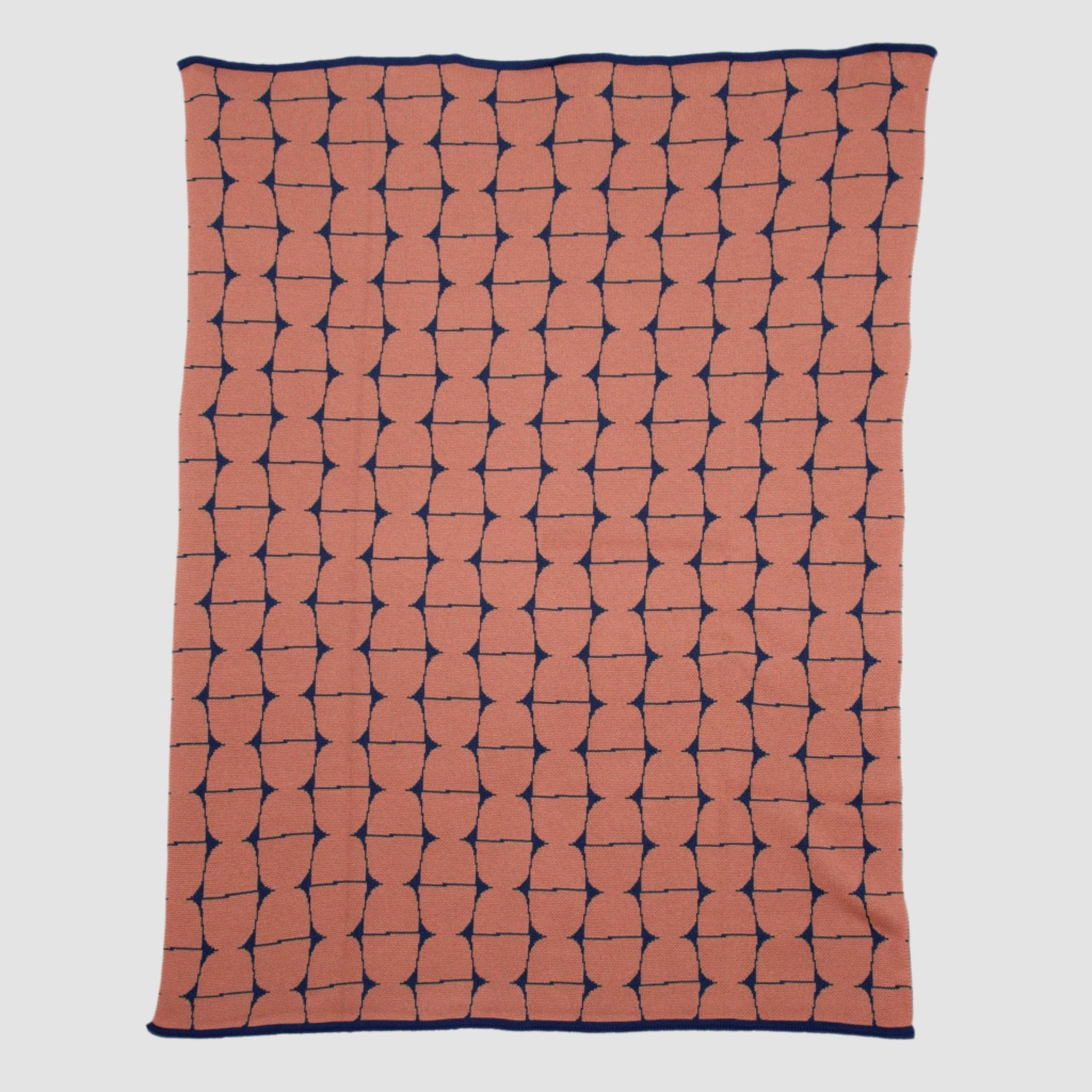 The Poly Kaarna Throw Blanket by Petra Kaksonen for in2green features a minimalist Scandinavian design with interconnected black shapes on a dusty rose background. Made from recycled polyester, it offers an eco-friendly touch.