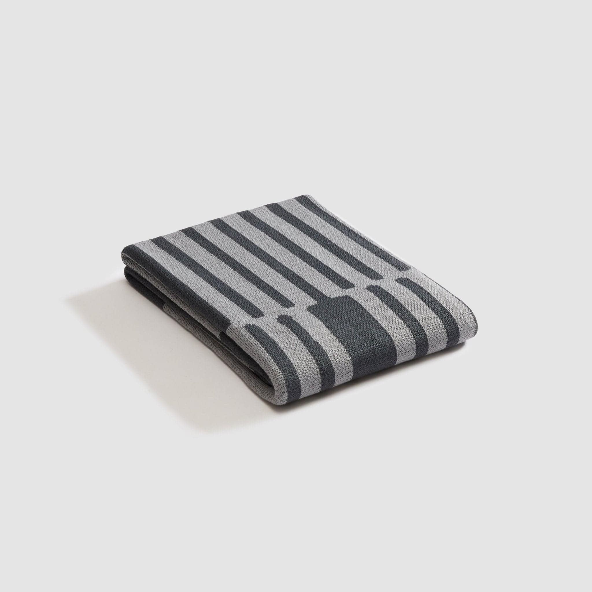 Part of in2green's Outdoor Collection, the Poly Retki Throw Blanket by Petra Kaksonen features folded striped patterns in dark and light gray on a plain background, made from recycled polyester.
