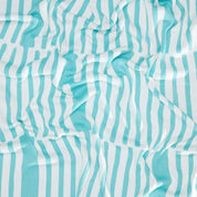 The Poly Retki Throw Blanket by Petra Kaksonen from in2green's outdoor collection showcases a crumpled fabric design with teal and white vertical stripes, crafted from recycled polyester.