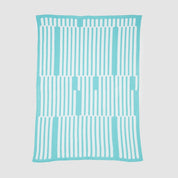 The Poly Retki Throw Blanket by Petra Kaksonen from in2green is part of the Kaareva outdoor collection. It features a turquoise design with vertical white stripes, crafted from recycled polyester for an eco-friendly touch, and lays flat on a white background.