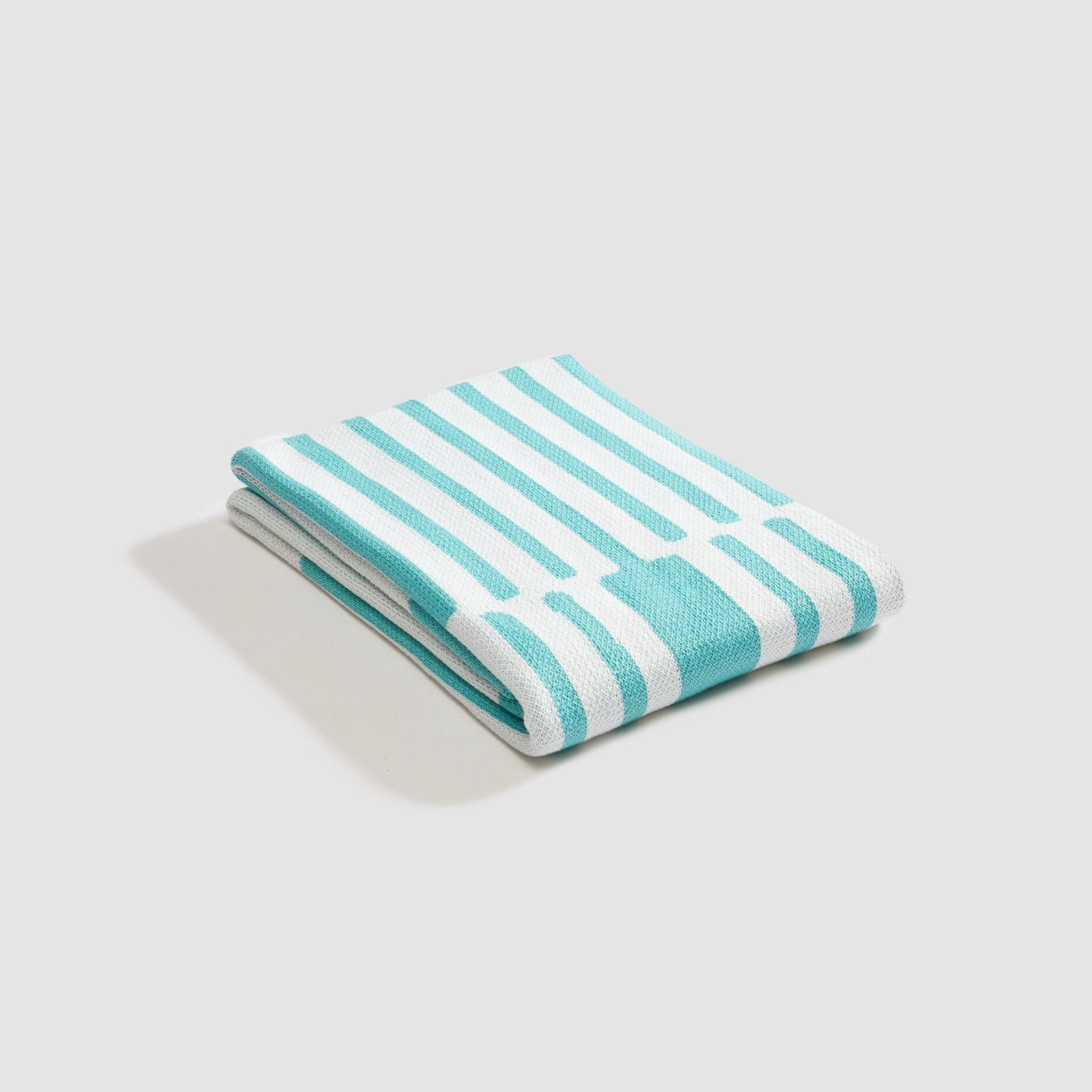 The Poly Retki Throw Blanket by Petra Kaksonen from in2green features a neatly folded turquoise and white stripe design, crafted from recycled polyester. Part of the exclusive Outdoor Collection, it combines eco-friendly materials with stylish flair on a plain light background.