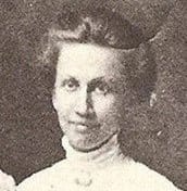 A black and white photo captures a woman with short hair in a high-collared blouse, exuding elegance as the fabric drapes luxuriously like the refined Prairie Rose Throw Blanket by Hannah Borger Overbeck from in2green’s recycled cotton blend collection.