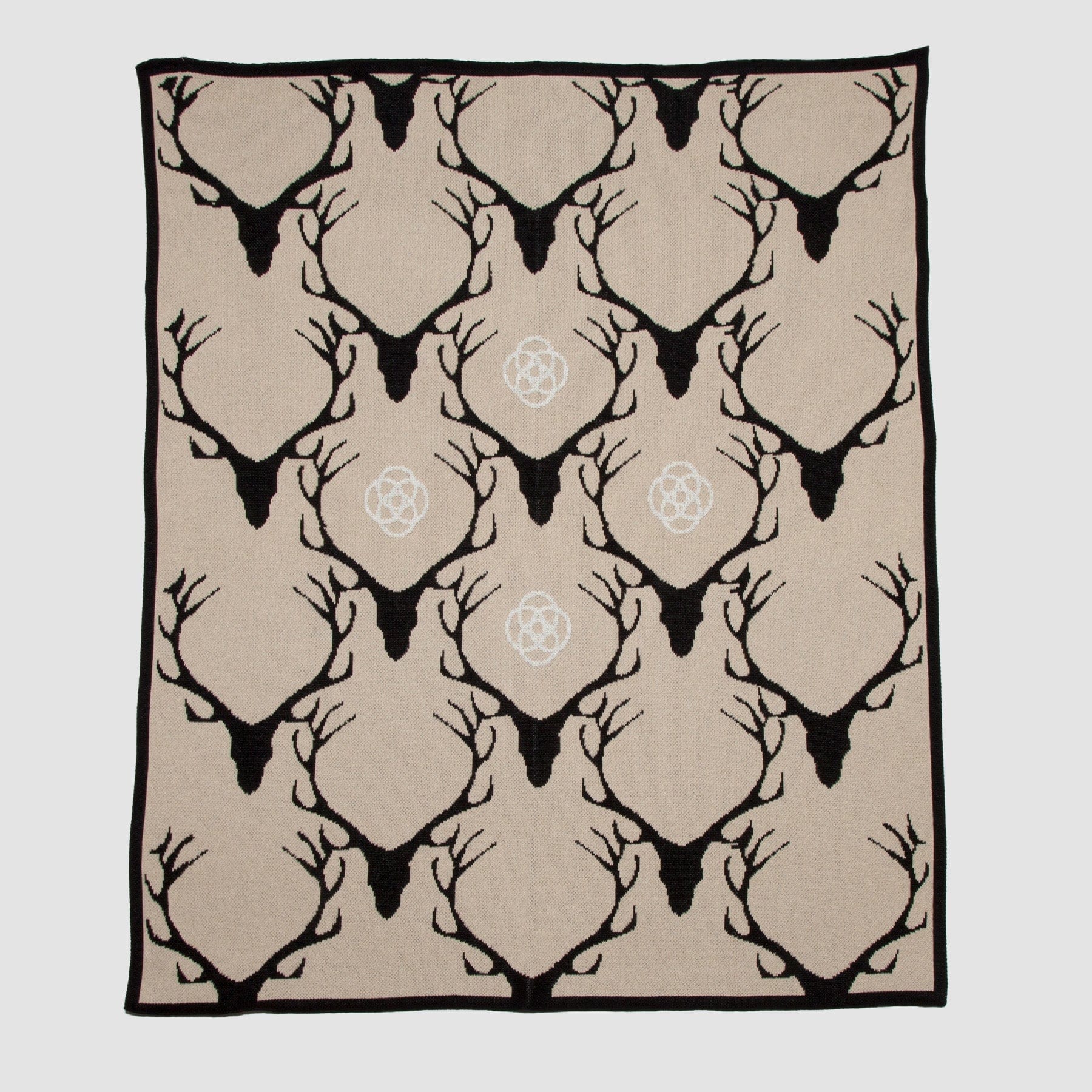 The Stag Longhorn Throw Blanket by in2green showcases black antlers and head silhouettes on tan, accented with white symbols. This nature-inspired blanket provides warmth and comfort, perfect for any cozy setting.