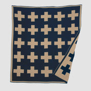 The Swiss Cross Reversible Throw Blanket by in2green has a reversible design with beige plus signs on dark blue, enhancing any ski chalet elegantly. Its neatly folded corners ensure a cozy look.