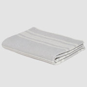 Introducing the Woven Twill Blanket by in2green, a folded gray throw crafted from recycled cotton and featuring elegant light stripe patterns.