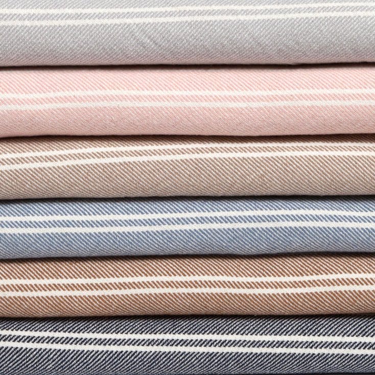 A collection of Woven Twill Blankets by in2green, featuring striped patterns in a range of colors such as gray, pink, beige, blue, and brown, crafted from eco yarns.