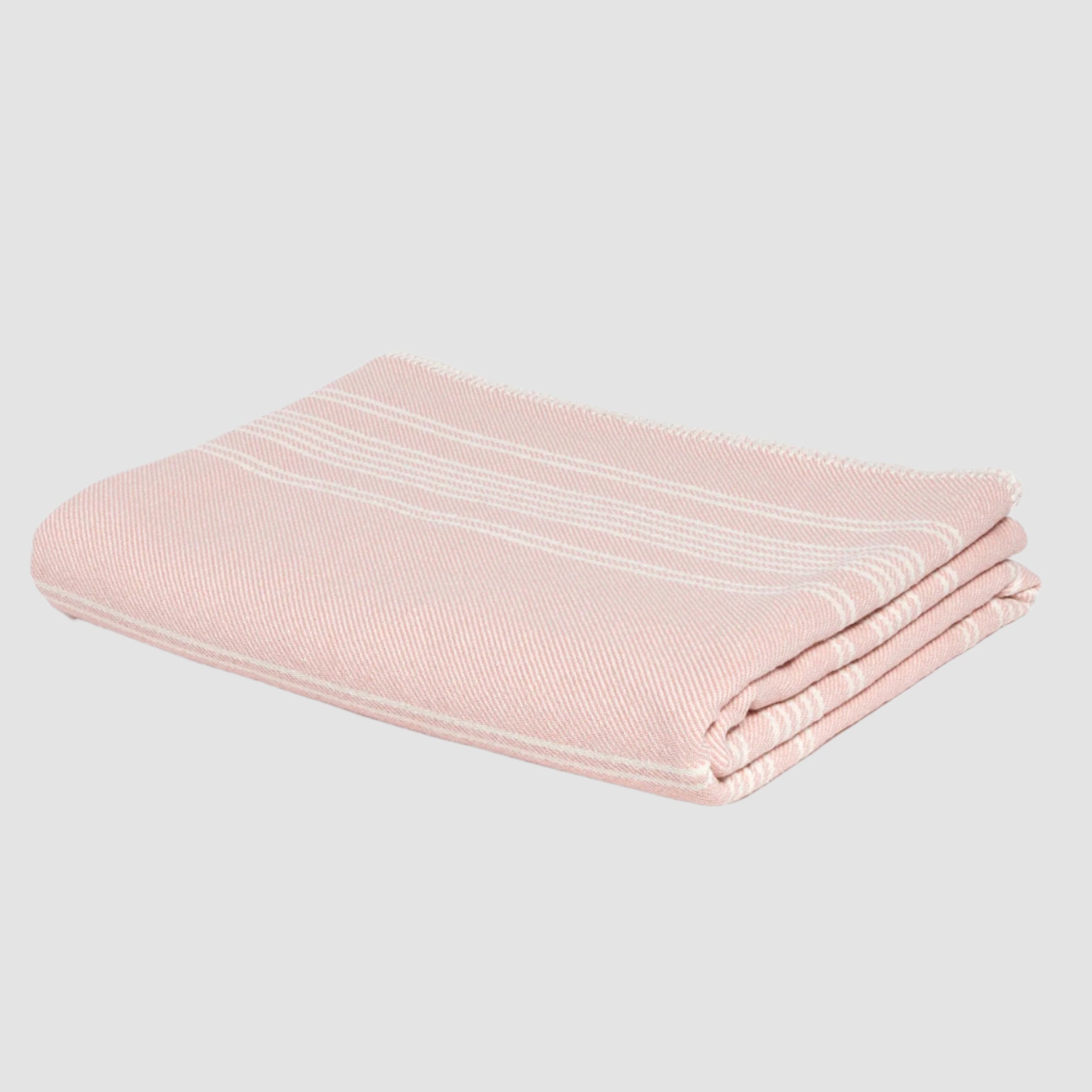 Against a white backdrop, the in2green Woven Twill Blanket, crafted from recycled cotton, displays its neatly folded design in light pink with thin white stripes.