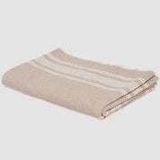 The Woven Twill Blanket by in2green beautifully combines sustainability and style with its folded beige and white striped design and fringed edges, made from recycled cotton.