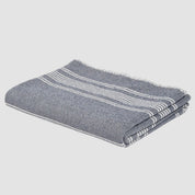 The in2green Woven Twill Blanket, featuring folded gray fabric with white stripes and made from eco yarns and recycled cotton, is displayed against a white background.