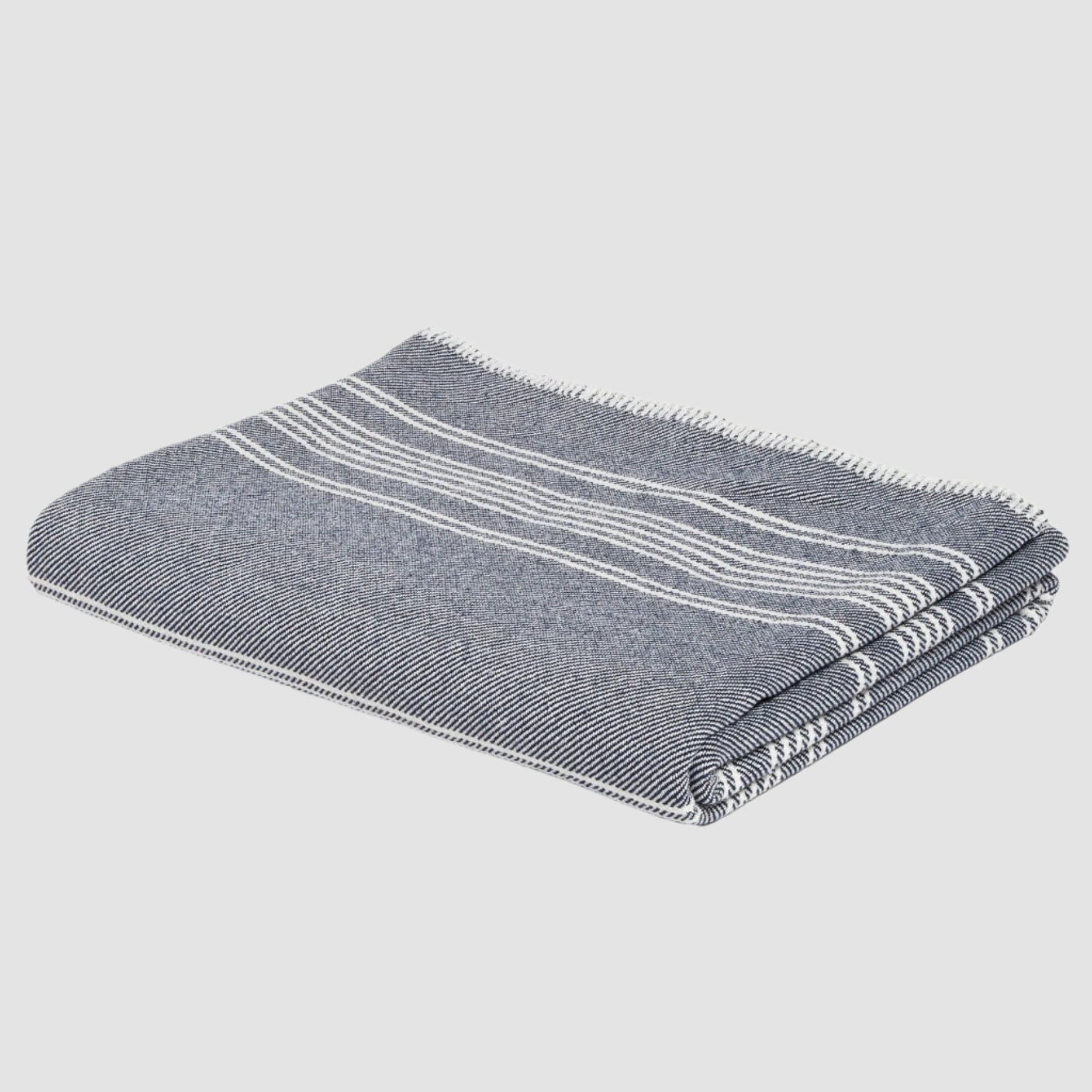 The in2green Woven Twill Blanket, featuring folded gray fabric with white stripes and made from eco yarns and recycled cotton, is displayed against a white background.