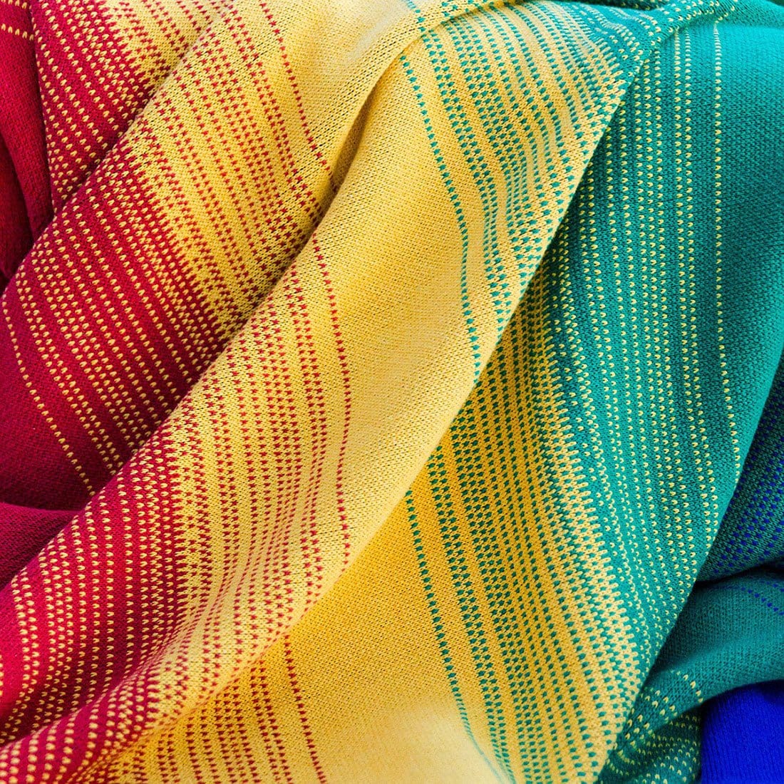 A close-up of woven fabric with red, yellow, green, and blue sections, featuring intricate dotted and striped patterns. The fabric is arranged in gentle folds, showcasing its texture.