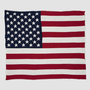 The image displays the Hometown Pride Flag - Cotton Sustainable Knit Blanket by in2green, showcasing the United States flag with thirteen red and white stripes and fifty white stars on a blue field in the upper left corner, beautifully crafted in the USA.