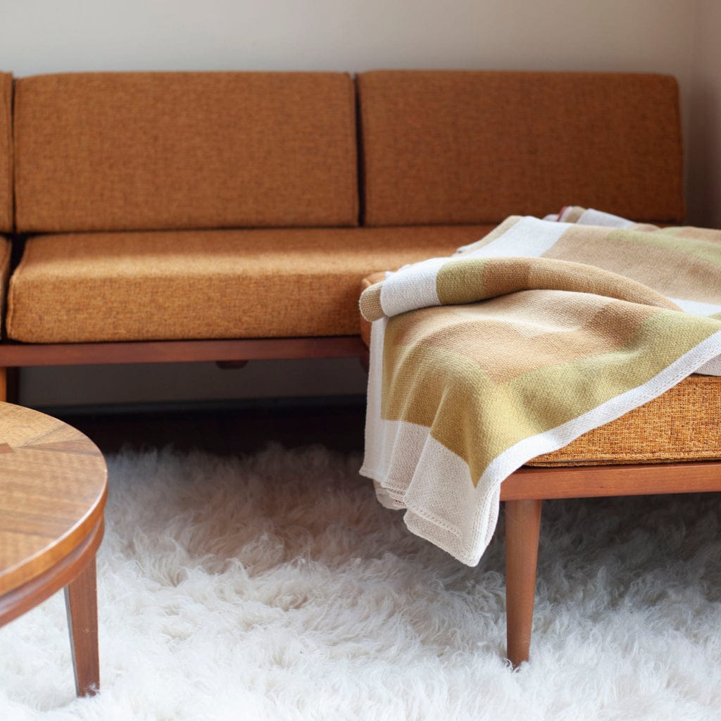 Brown sofa with a yellow Bauhaus inspired blanket draped over it on a white carpet