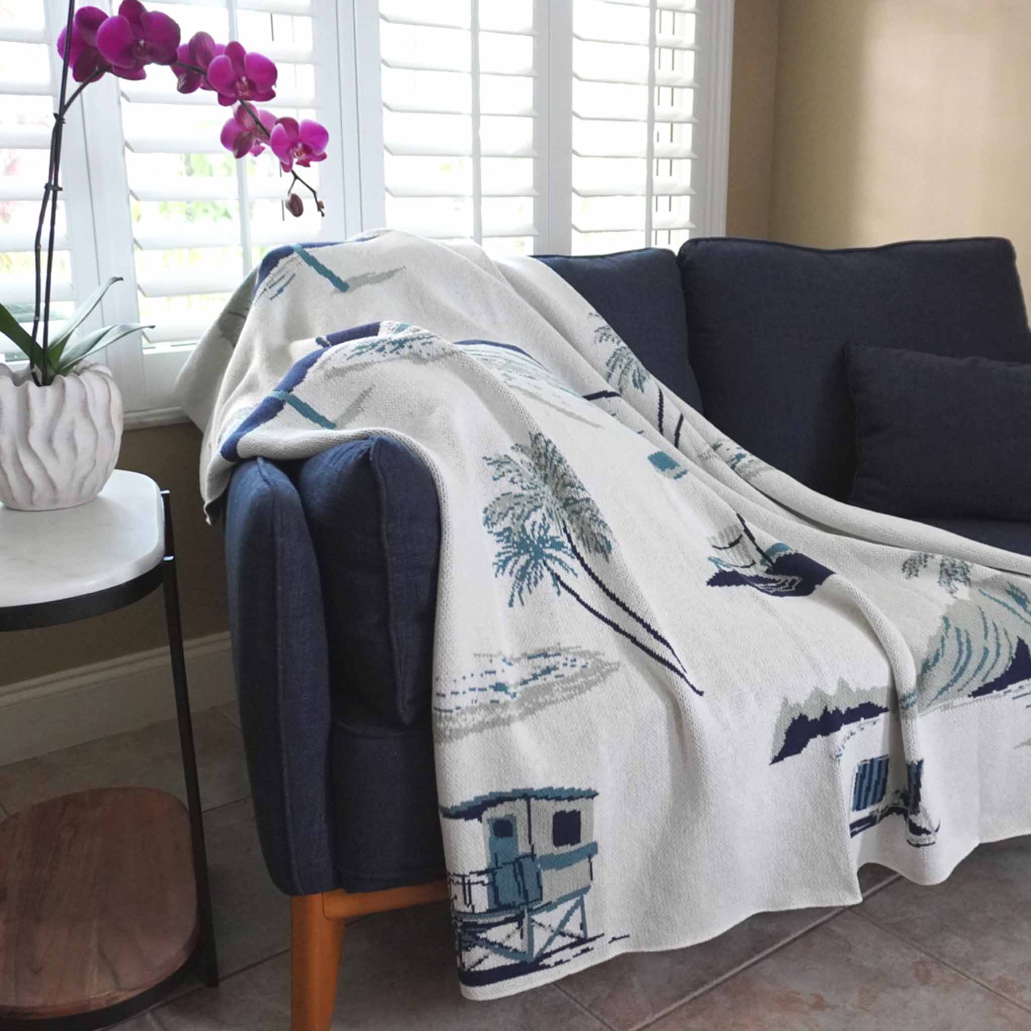 beach toile blanket draped over a dark blue couch in a living room.