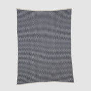 The Broken Zig Zag Throw Blanket showcases a repeating black and white chevron pattern, crafted from recycled cotton yarns for a sustainable addition to modern decor.