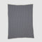 The Broken Zig Zag Throw Blanket showcases a repeating black and white chevron pattern, crafted from recycled cotton yarns for a sustainable addition to modern decor.
