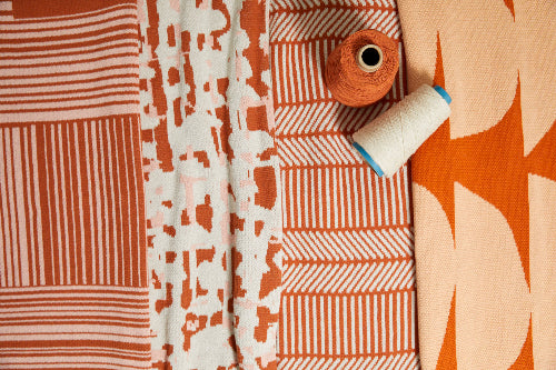 Blankets of various patterns with orange colors accompanied by spools of orange and white yarn.